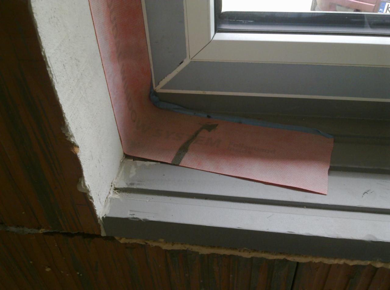 Montaż okna z użyciem czerwonej membrany uszczelniającej, widoczne detale łączenia z murem z cegły dziurawki.