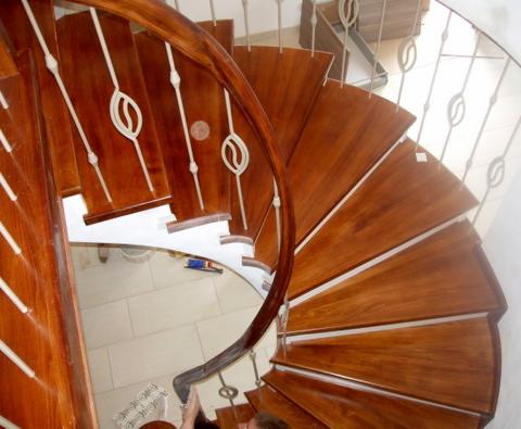 Wysoki kąt widzenia na spiralne schody z drewna egzotycznego z ozdobnymi, metalowymi balustradami, w trakcie montażu, widoczne narzędzia i niedokończone wykończenie.