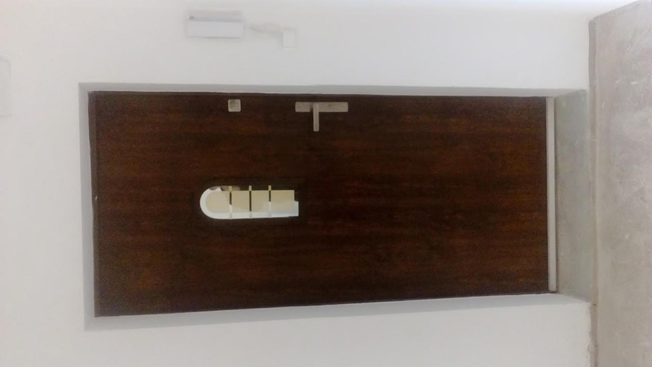 Ciemnobrązowe, drewniane okienko rewizyjne z metalowym zamknięciem, wstawione w białą ścianę, z widoczną białą ramą wokół i szarą ścianą w rogu.