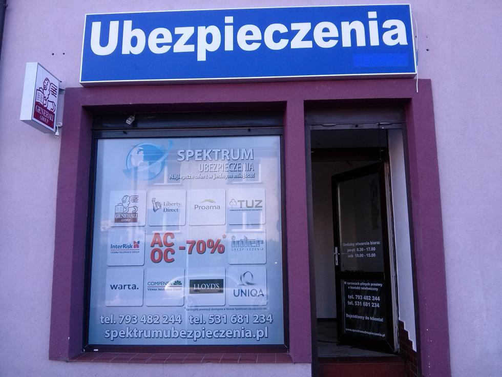 Fasada biura ubezpieczeń Spektrum z logotypami firm ubezpieczeniowych na witrynie i godzinami otwarcia na drzwiach, fioletowa elewacja, niebieski szyld.