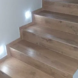 Schody wykończone panelami imitującymi drewno, z oświetleniem punktowym w ścianie, widok z dołu.