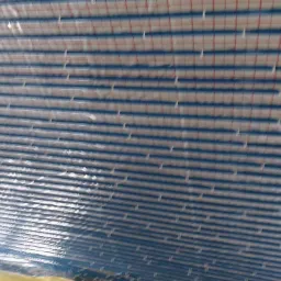 Folia izolacyjna z niebieską siatką i czerwonymi liniami, rozłożona na podłożu, widoczne fragmenty żółtej taśmy montażowej.