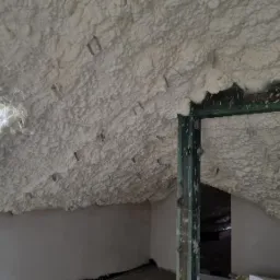 Poddasze po natrysku pianki izolacyjnej PUR, widoczne metalowe kotwy mocujące, okno dachowe i fragment ramy drzwiowej.