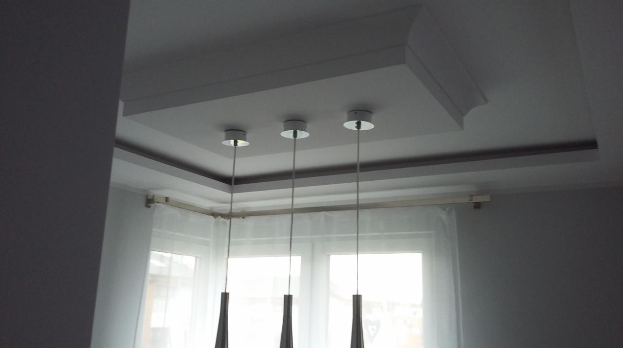 Biały sufit podwieszany z trzema nowoczesnymi lampami wiszącymi, widok z dołu, okno w tle, szare ściany.