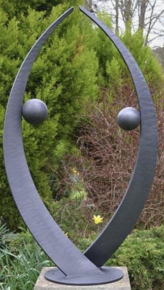 Nowoczesna, metalowa rzeźba ogrodowa z dwoma kulami, w Lubinie, na tle zieleni.