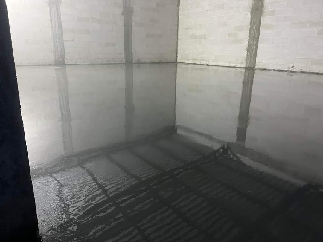 Świeżo wylana, mokra posadzka przemysłowa w surowym wnętrzu z bloków betonowych, widoczne zarysy ogrzewania podłogowego.