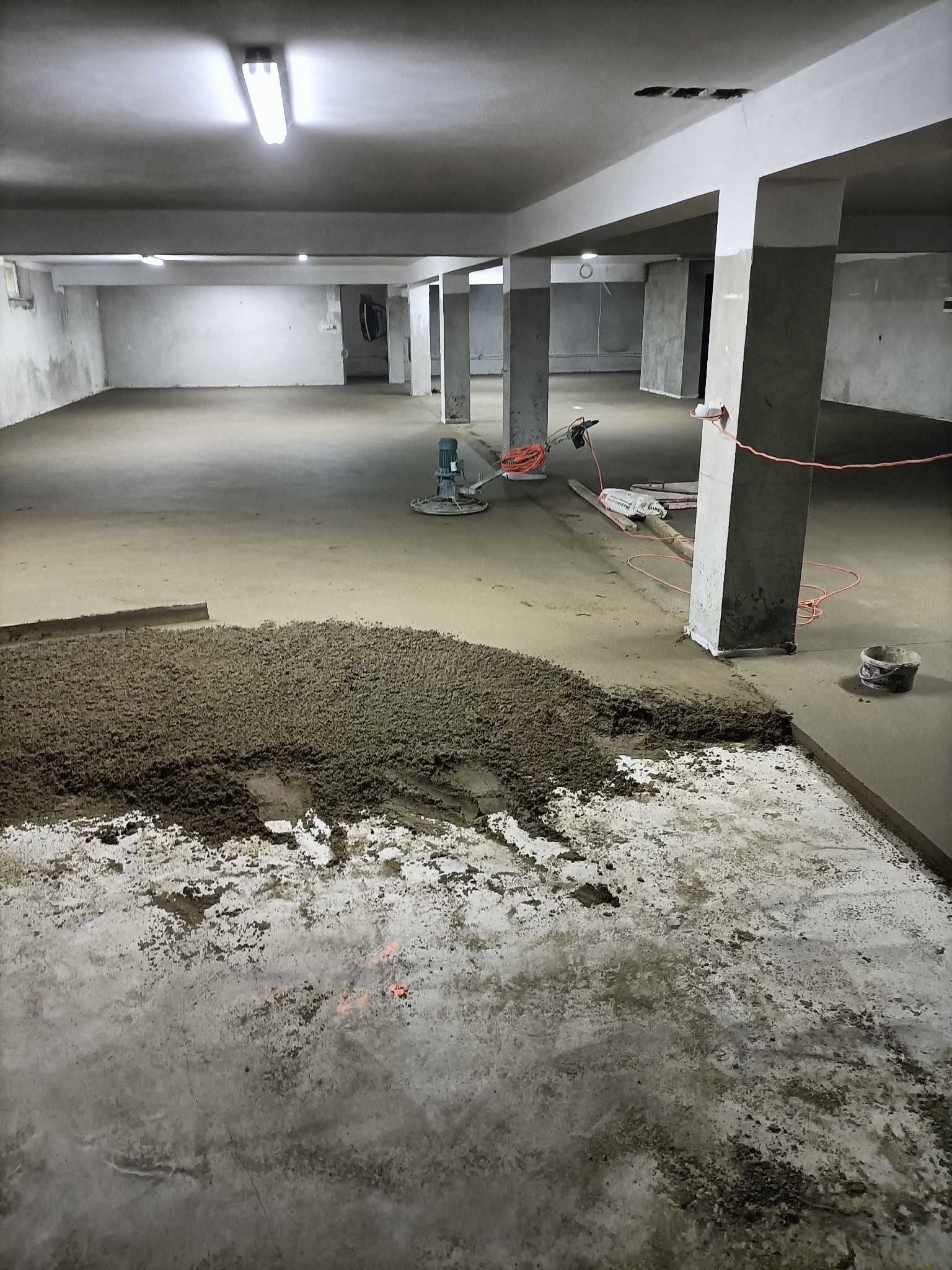 Wylewka betonowa w hali przemysłowej w trakcie realizacji, widoczny agregat tynkarski, świeżo wylany beton i fragment wygładzonej posadzki.