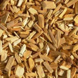 Jasne, drobne zrębki drzewne ułożone gęsto, wypełniające całą przestrzeń kadru. Widoczne różne odcienie brązu i beżu, struktura drewna wyraźnie zarysowana.