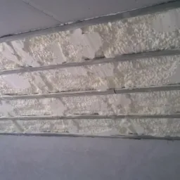 Izolacja poddasza pianką: biała pianka szczelnie wypełnia przestrzeń między metalowymi profilami, tworząc warstwę termoizolacyjną.