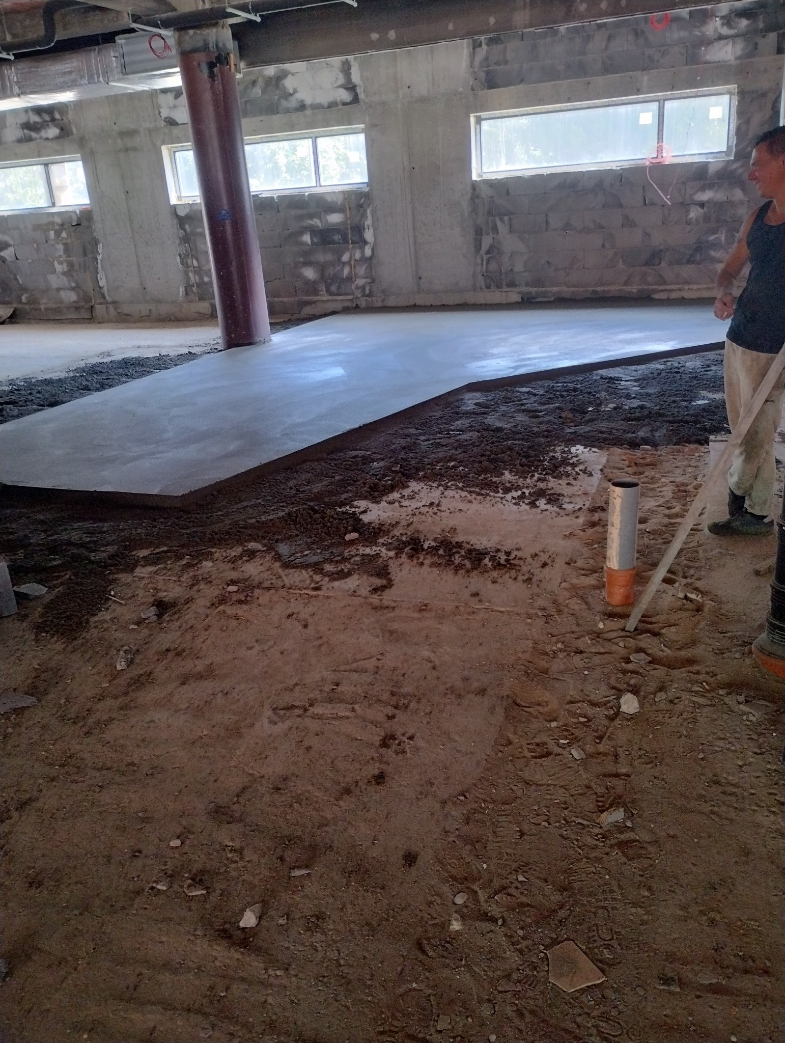 Wylewka betonowa w surowym stanie, częściowo pokryta zaprawą, widoczny pracownik z łopatą, w tle okna i betonowe ściany.