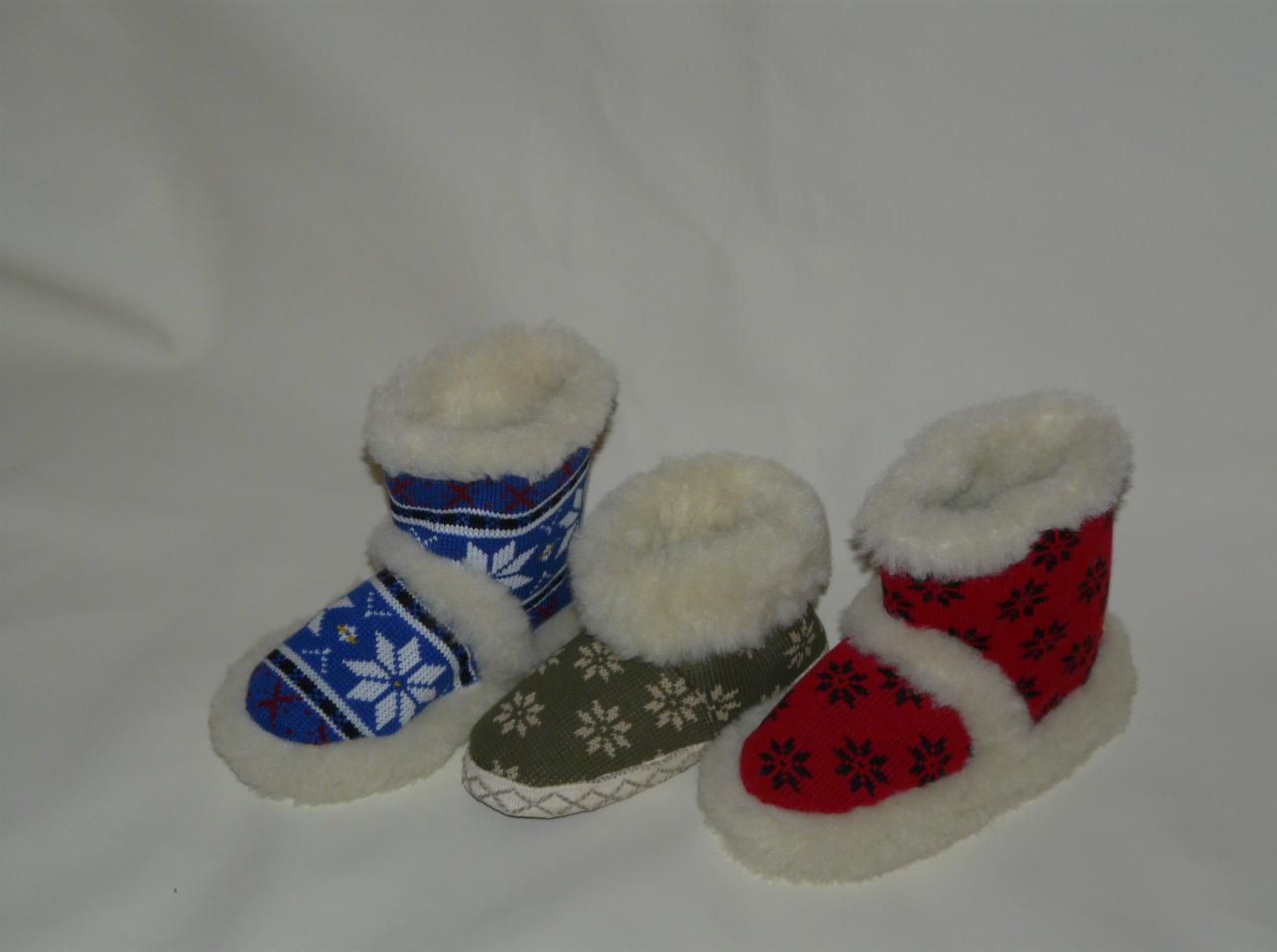 Trzy pary ręcznie robionych, kolorowych kapci-botków z motywem śnieżynek i futrzanym wykończeniem, ustawione obok siebie na jasnym tle.