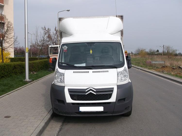 Biały samochód dostawczy Citroen z zabudową kontenerową, zaparkowany na poboczu, z otwartymi drzwiami kabiny pasażera, widok z przodu.