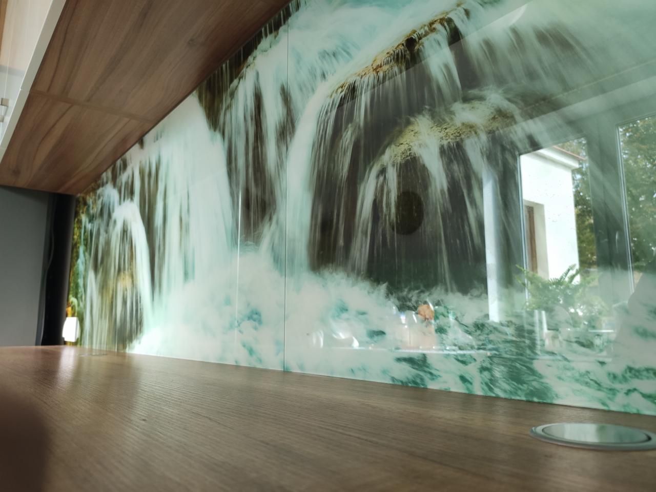Szklany panel ścienny w kuchni z nadrukowanym motywem wodospadu, widok z bliska na blat i fragment okna.
