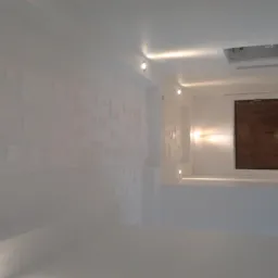 Białe wnętrze po remoncie: ściana z dekoracyjnymi panelami 3D, punktowe oświetlenie sufitowe, widoczna wnęka z drewnianym elementem dekoracyjnym.