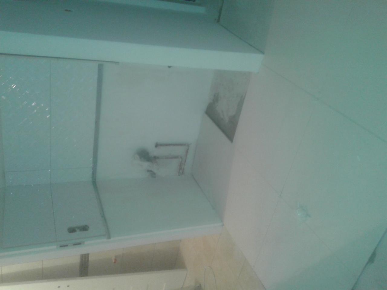 Biała łazienka w trakcie remontu: widoczne płytki na ścianach i brodziku, instalacja wodna przygotowana do podłączenia armatury, fragment sufitu podwieszanego.