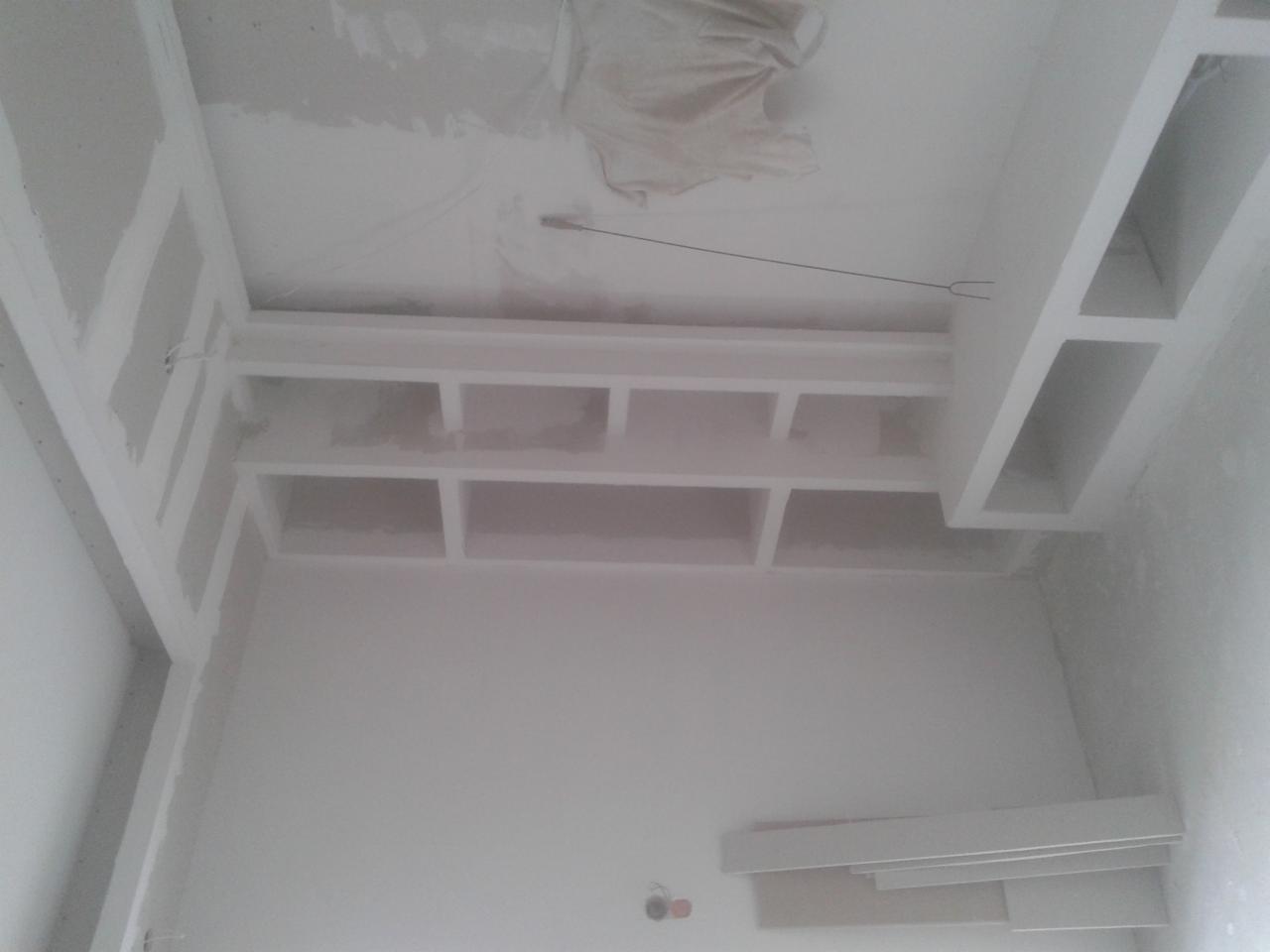Białe, surowe wnętrze z zabudową z płyt gipsowych na suficie, widok z dołu. Elementy konstrukcyjne w trakcie prac wykończeniowych, widoczne ślady szpachlowania.