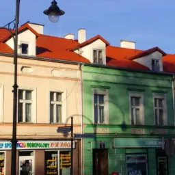 Fasady trzech kamienic o różnej kolorystyce z czerwonymi dachami, widoczne z poziomu ulicy, oświetlone światłem dziennym. Charakterystyczna architektura miejska.