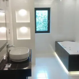 Nowoczesna łazienka z białą armaturą, czarnymi akcentami, podświetleniem LED i oknem z widokiem na zieleń.