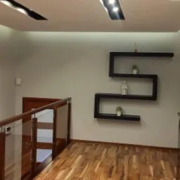 Korytarz w domu z drewnianą podłogą, szklaną balustradą, ścianą z białej cegły i p&oacute;łkami w kształcie litery S z dekoracjami.