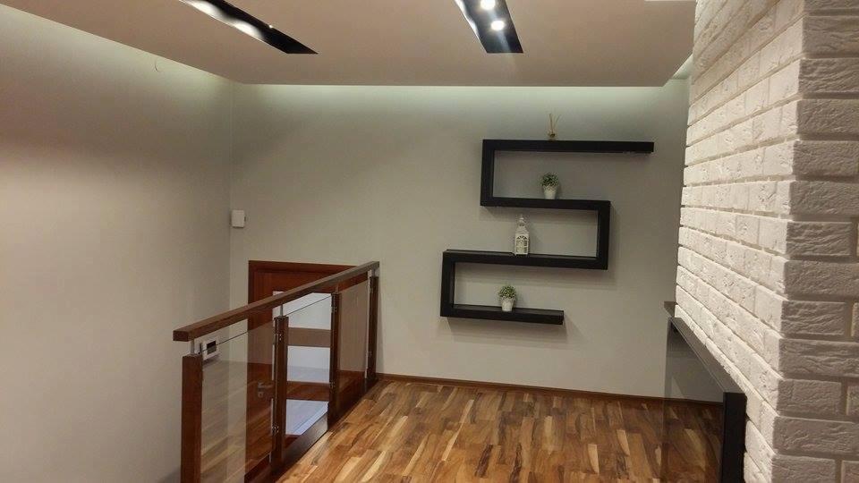 Korytarz w domu z drewnianą podłogą, szklaną balustradą, ścianą z białej cegły i półkami w kształcie litery S z dekoracjami.
