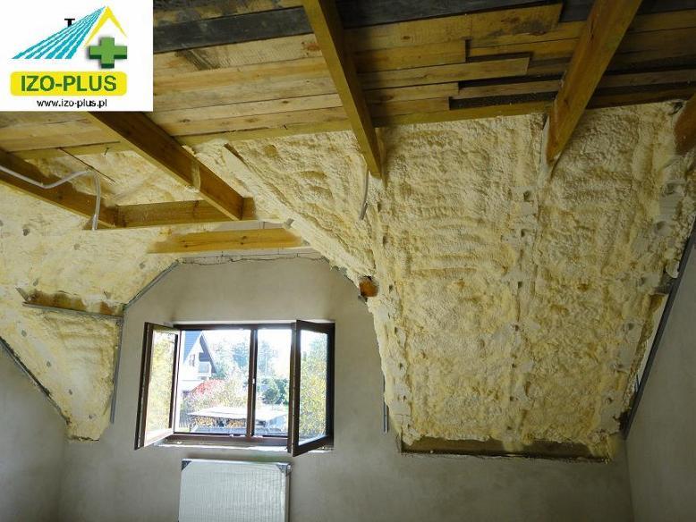 Poddasze po ociepleniu pianką PUR, widoczne drewniane elementy konstrukcyjne i otwarte okno z widokiem na zieleń. Aplikacja pianki o nieregularnej strukturze.