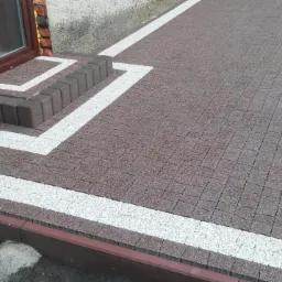 Ułożona kostka brukowa w odcieniach brązu z białymi pasami, tworząca wzór przy schodach i wzdłuż krawędzi, z widocznymi schodami z kostki.