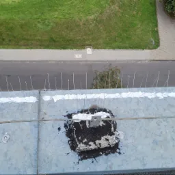 Metalowy dach z zamontowanymi kolcami przeciw ptakom, uszczelnionymi białą masą. Widok z góry na ulicę i zieleń. Zabezpieczenie przed ptactwem na dachu budynku.