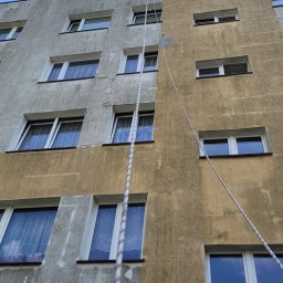 NO LIMIT Damian Krzesak - Budynek z elewacją w połowie wyczyszczoną, widoczna różnica między brudną a czystą częścią. Lina pionowo wzdłuż ściany. Ujęcie z dołu, niebo w tle.