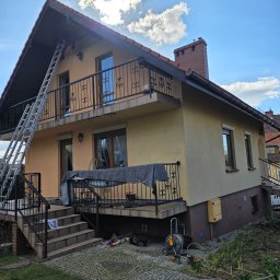 NO LIMIT Damian Krzesak - Dom z balkonem w trakcie malowania elewacji. Rozstawiona drabina, widoczne narzędzia i farby. Część elewacji pomalowana na ciemniejszy odcień.