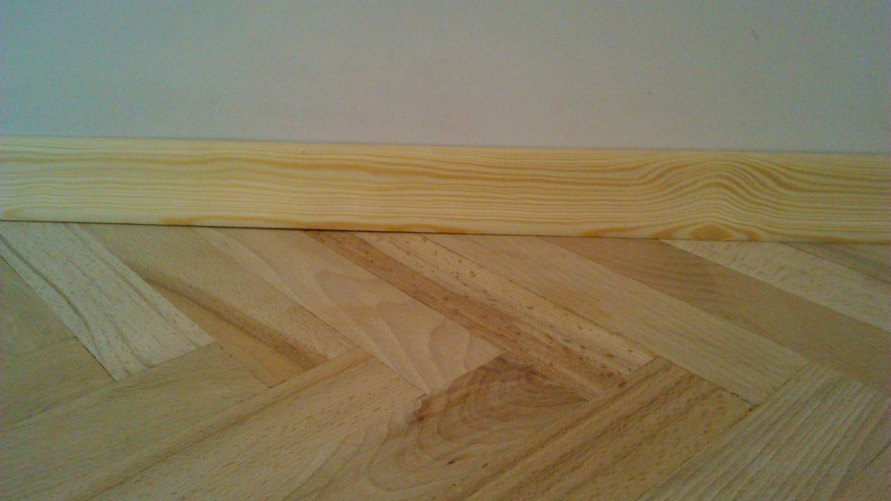 Parkiet ułożony w jodełkę z zamontowaną surową, drewnianą listwą przypodłogową przed malowaniem.