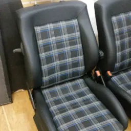 Dwa samochodowe fotele, czarna skóra z szarą kratą w niebieską linię, zagłówek i regulacja oparcia, widok z bliska na podłodze.