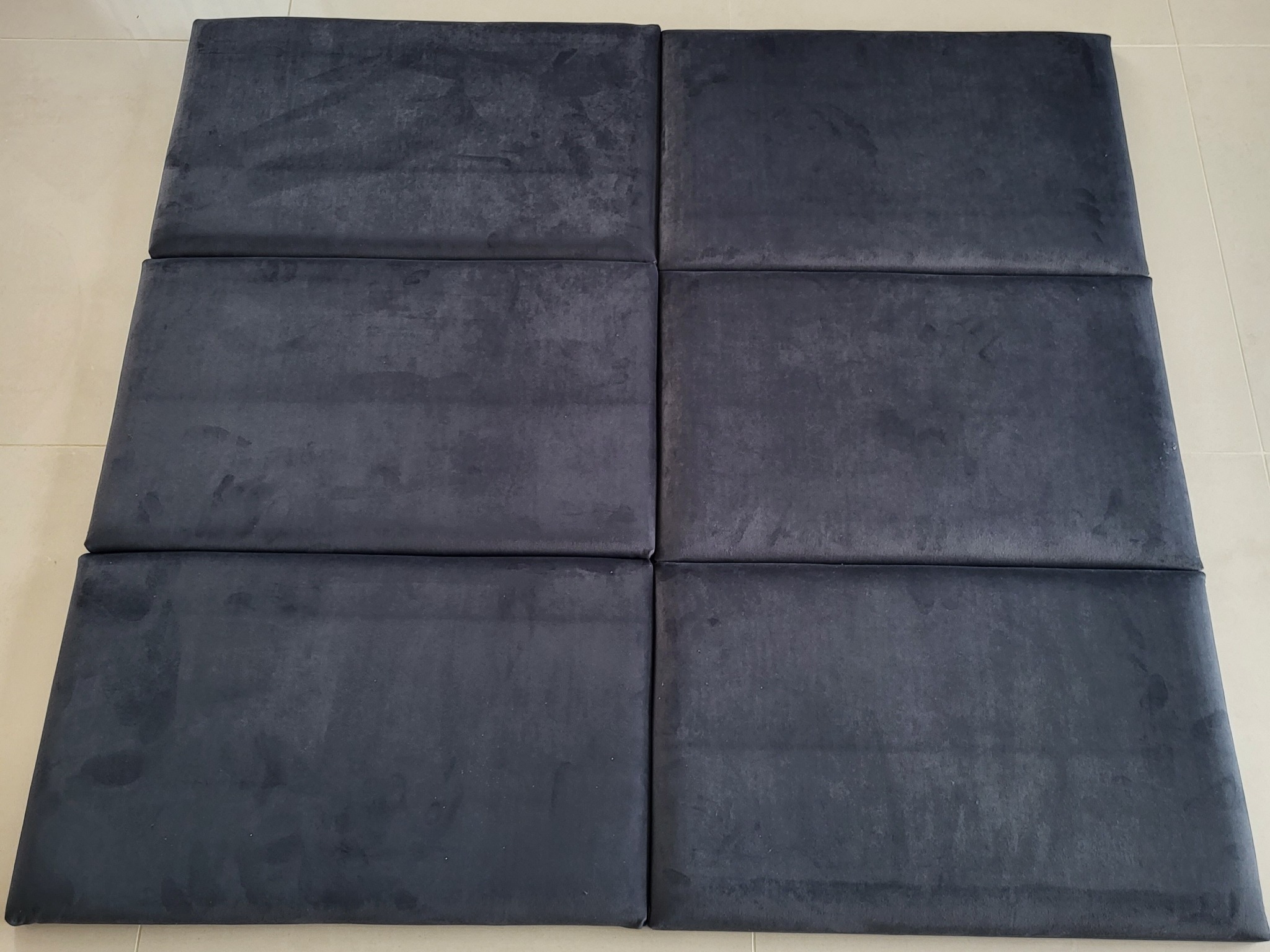 Sześć ciemnych, welurowych paneli tapicerowanych ułożonych na podłodze z jasnych płytek, tworzących prostokątną powierzchnię.