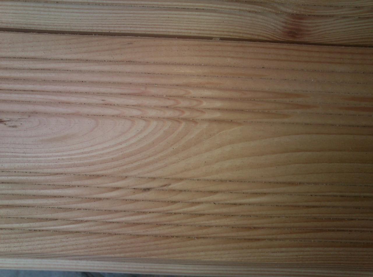 Surowe deski sosnowe z widocznym usłojeniem, ułożone jedna na drugiej, z delikatnym cieniem na dolnej części.