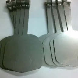 Partie metalowych, szlifowanych elementów z uchwytami w kształcie pierścieni, ułożone w dwóch grupach na jasnym tle.