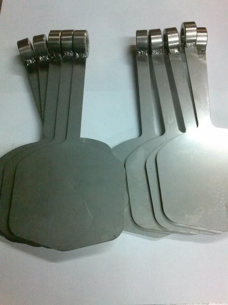 Partie metalowych, szlifowanych elementów z uchwytami w kształcie pierścieni, ułożone w dwóch grupach na jasnym tle.