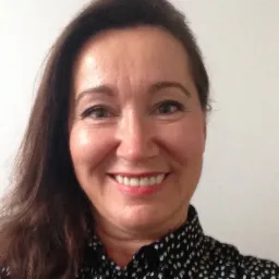 Portret uśmiechniętej kobiety z brązowymi włosami w czarno-białej bluzce, na jasnym tle, potencjalnie pracownik działu kadr.