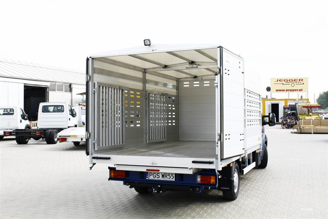 Biała zabudowa do przewozu zwierząt na samochodzie dostawczym z otwartymi kratami wentylacyjnymi, widok od tyłu na puste wnętrze, tablica rejestracyjna PGS WR55.