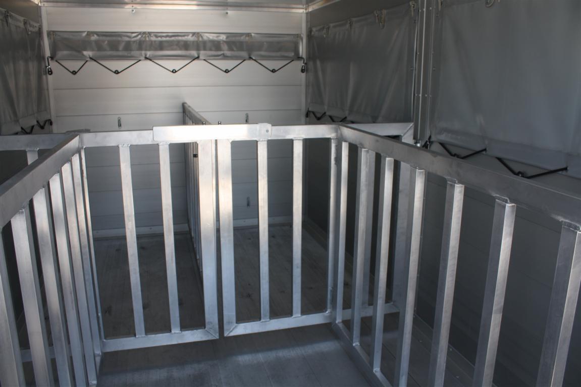 Wnętrze specjalistycznej zabudowy aluminiowej do transportu zwierząt w samochodzie dostawczym, widoczne przegrody z metalowych prętów, ściany wyłożone jasnym materiałem.