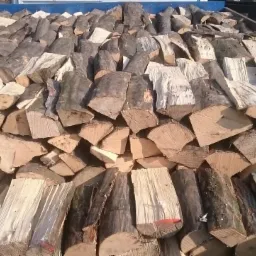 Stos pociętego drewna w skrzyni ładunkowej samochodu, widoczne fragmenty kory i jasnego drewna.