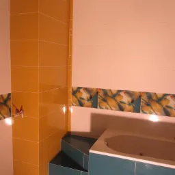 Wykończona łazienka z wanną, obłożona glazurą w odcieniach żółci i turkusu, z dekoracyjnym pasem kwiatowym. Widoczne schodki obłożone płytkami.