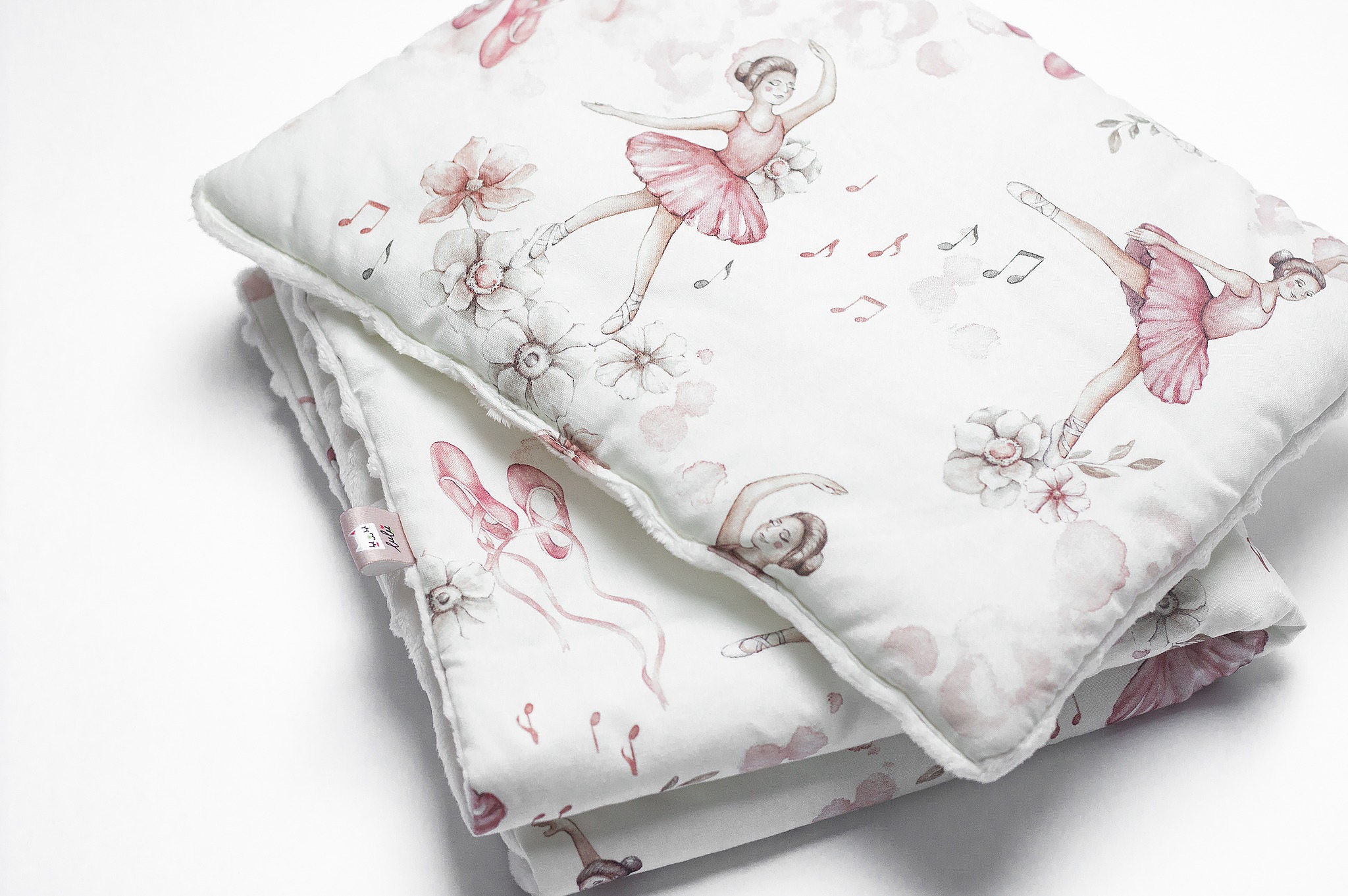 Stos poduszek dekoracyjnych z motywem baletnic i kwiatów na białym tle, wykończonych miękkim obszyciem, z widoczną metką producenta.