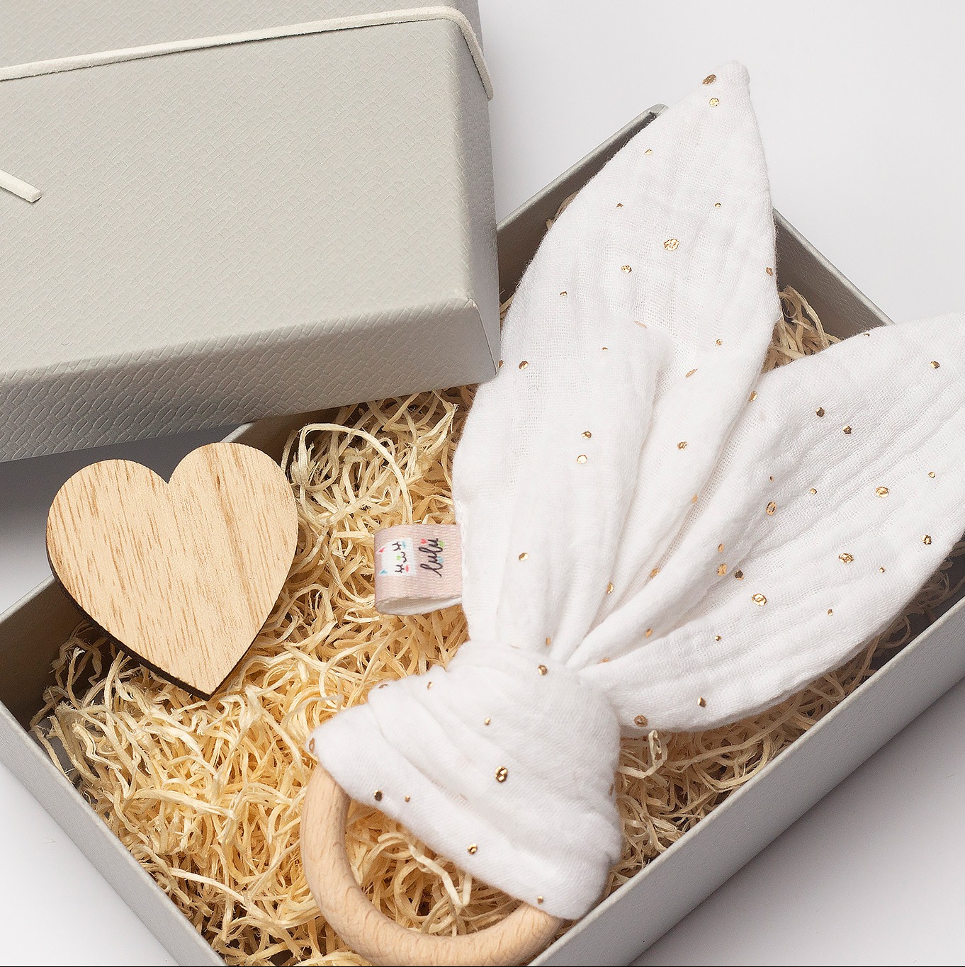Ręcznie szyty gryzak z uszami królika z muślinu w pudełku prezentowym z drewnianym sercem, idealny na prezent dla niemowlaka, w delikatnej kolorystyce.