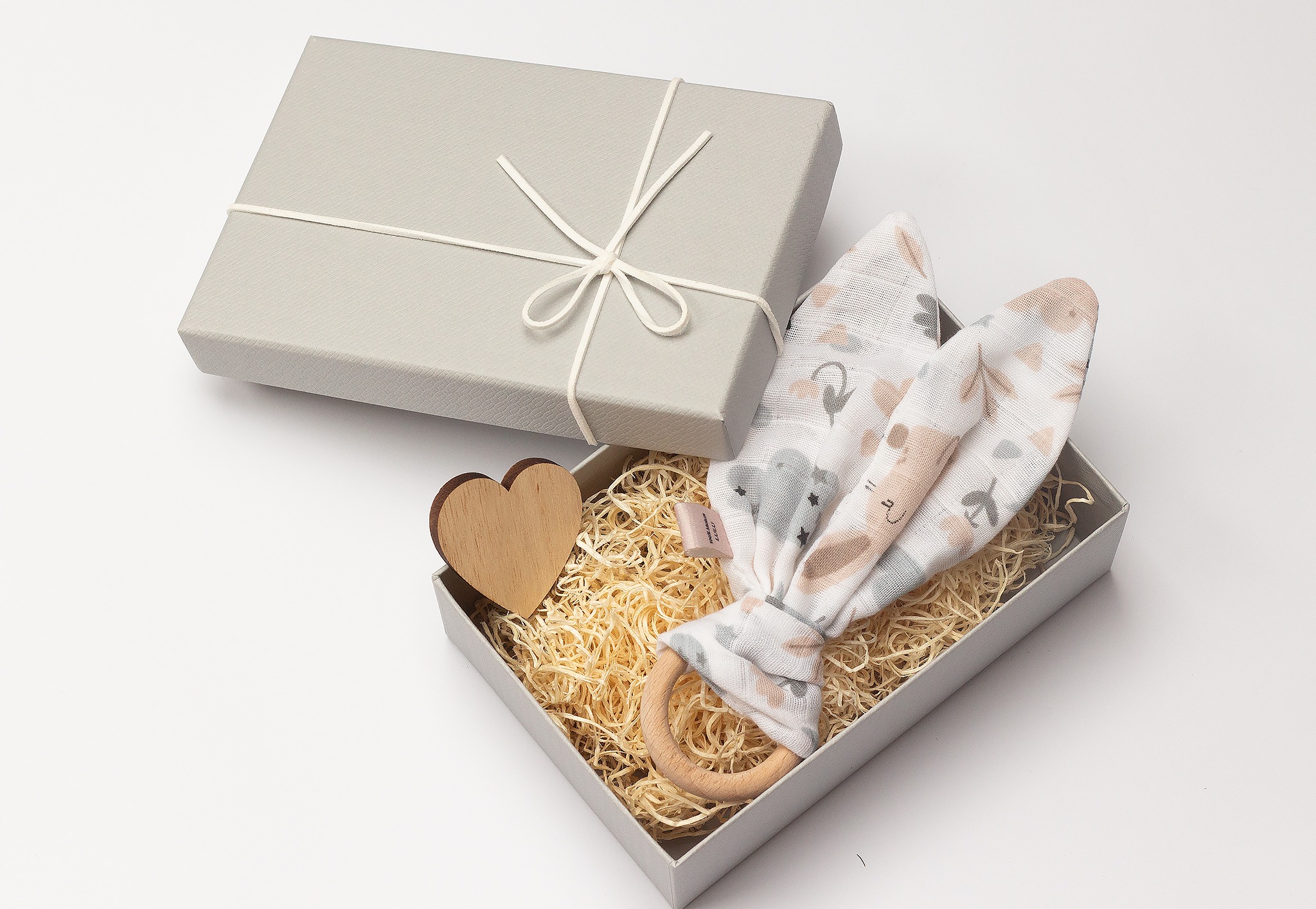 Elegancki, szary box z drewnianym sercem i zabawką z uszami królika wewnątrz, wypełniony siankiem. Idealny prezent dla dziecka, w neutralnej kolorystyce.