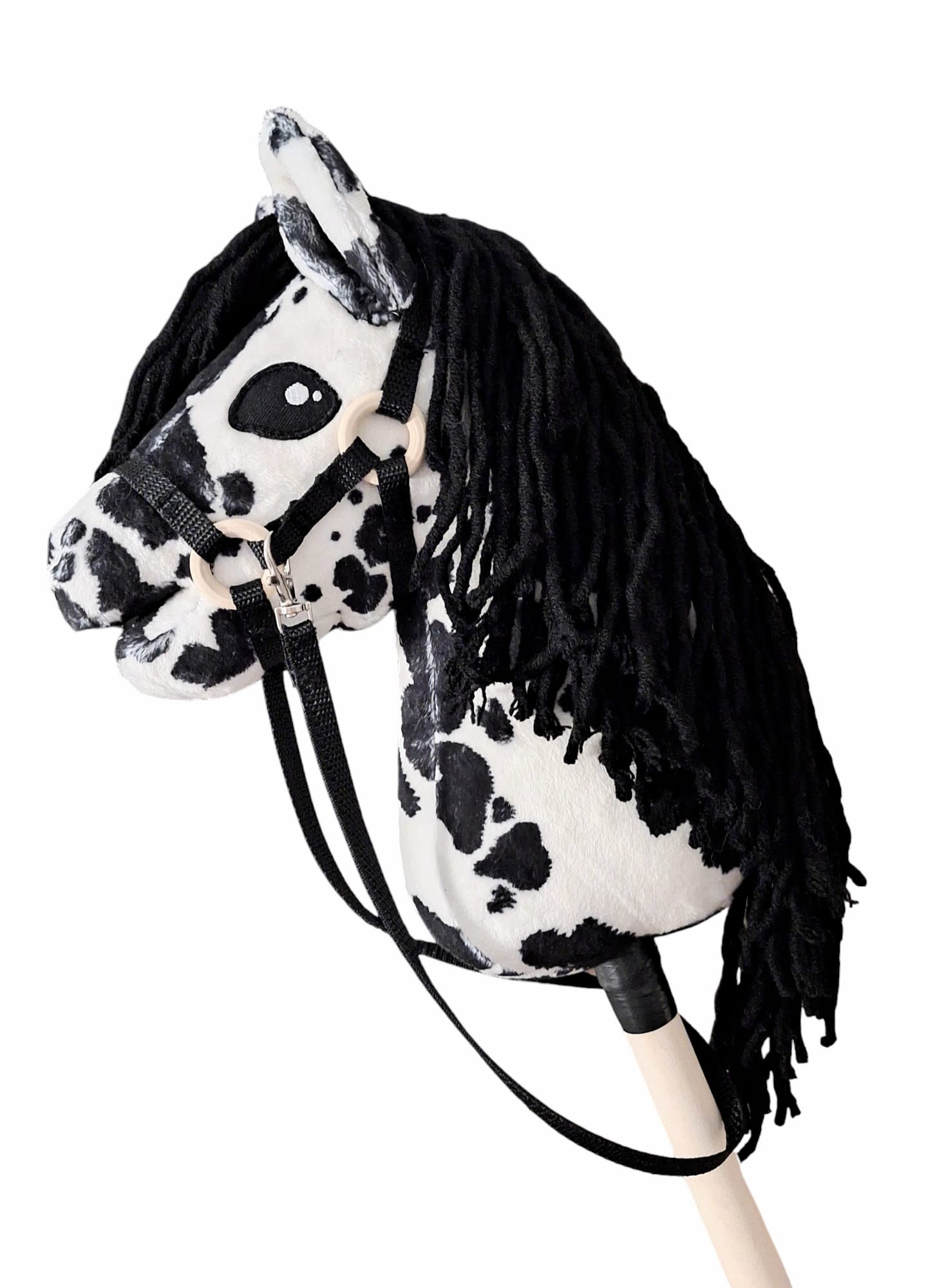 Pluszowy koń na kiju w biało-czarne łaty, z czarną grzywą z włóczki i czarnym kantarem, na jasnym tle. Zabawka dziecięca, rękodzieło.