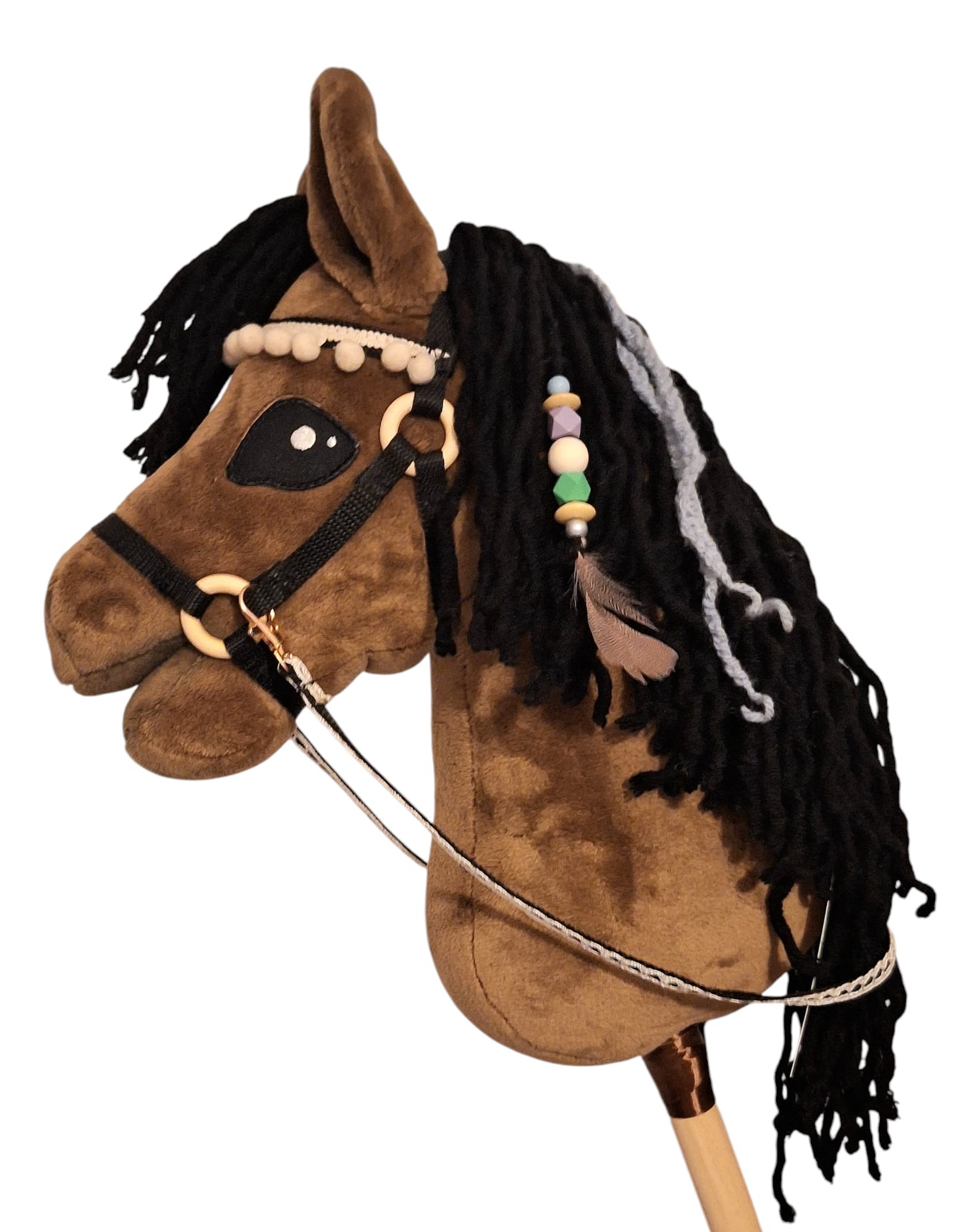 Pluszowy koń na kiju, brązowy z czarną grzywą, ozdobiony koralikami i piórkiem. Zabawka ma uzdę i charakterystyczne, naszywane oko.