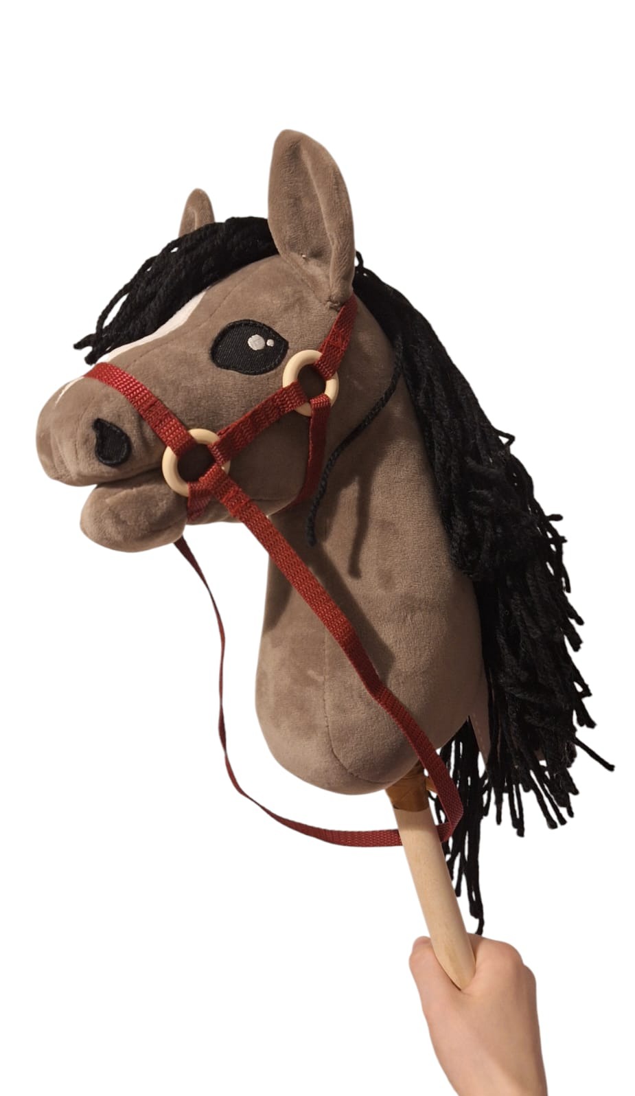 Szmaciana zabawka konik na kiju z brązową głową, czarną grzywą i czerwoną uprzężą, trzymana w ręku. Widok z bliska.
