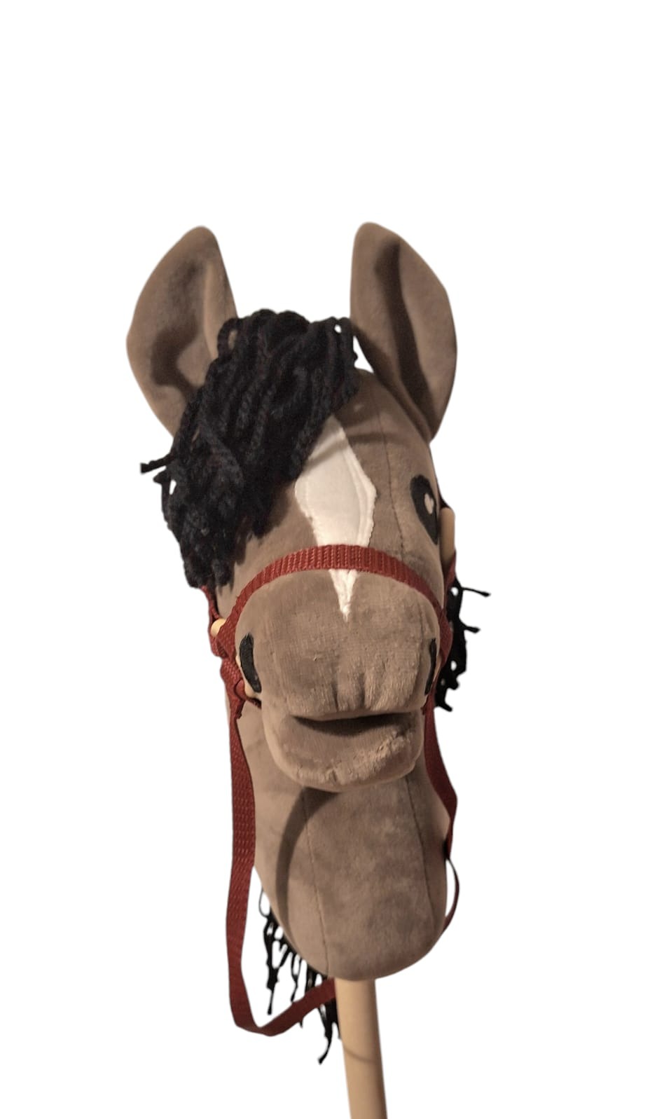 Pluszowy koń na kiju z brązową uprzężą i czarną grzywą, na białym tle. Zabawka dla dzieci, rękodzieło o miękkiej fakturze.