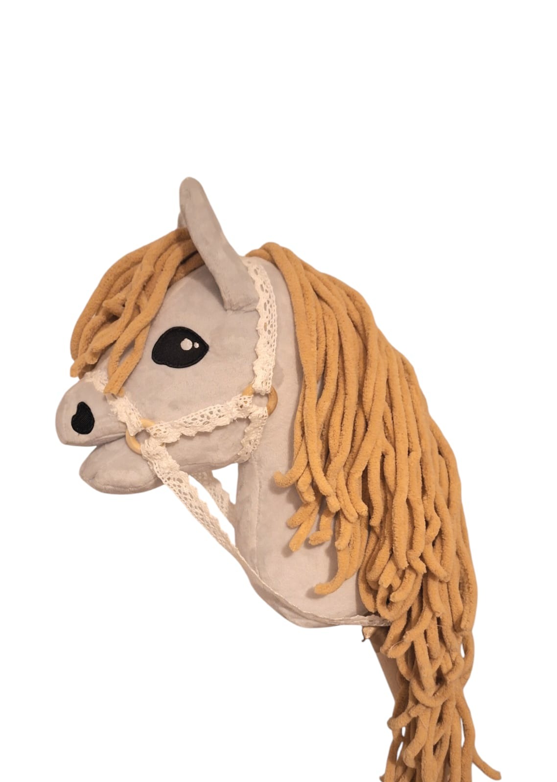 Pluszowa głowa konia na kiju, z grzywą z włóczki i ozdobnym kantarem z koronki, na białym tle. Zabawka w stylu handmade.