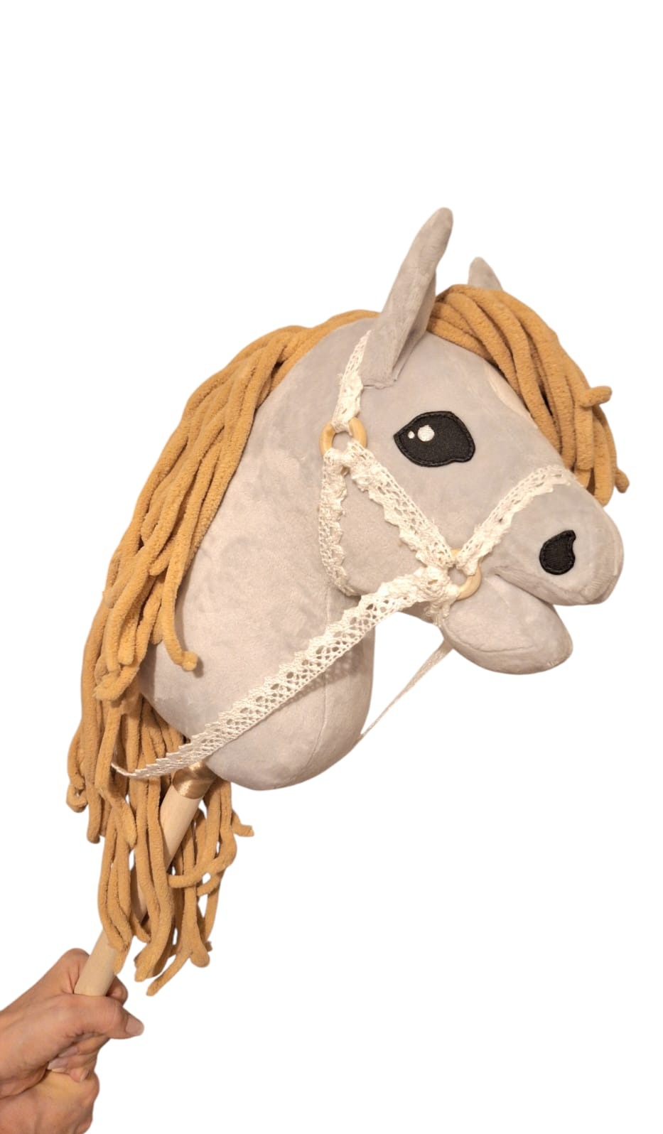 Pluszowy koń na kiju z beżową grzywą i ozdobnym kantarem z koronki, trzymany w dłoni. Zabawka ręcznie robiona, widoczny detal wykonania.