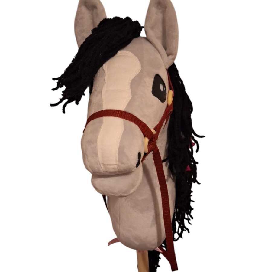 Szmaciana zabawka - koń na kiju, szary z czarną grzywą i czerwoną uprzężą, z bliska na białym tle. Ręcznie robiona zabawka.